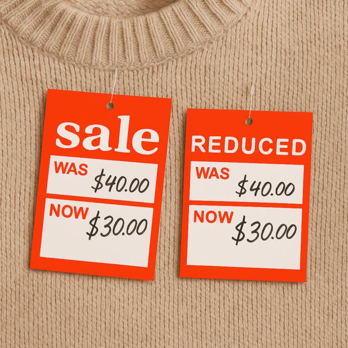 Red "SALE" and "REDUCED" tags punched into a beige sweater with a tagging gun, showing prices reduced from $40 to $30 in handwritten text.